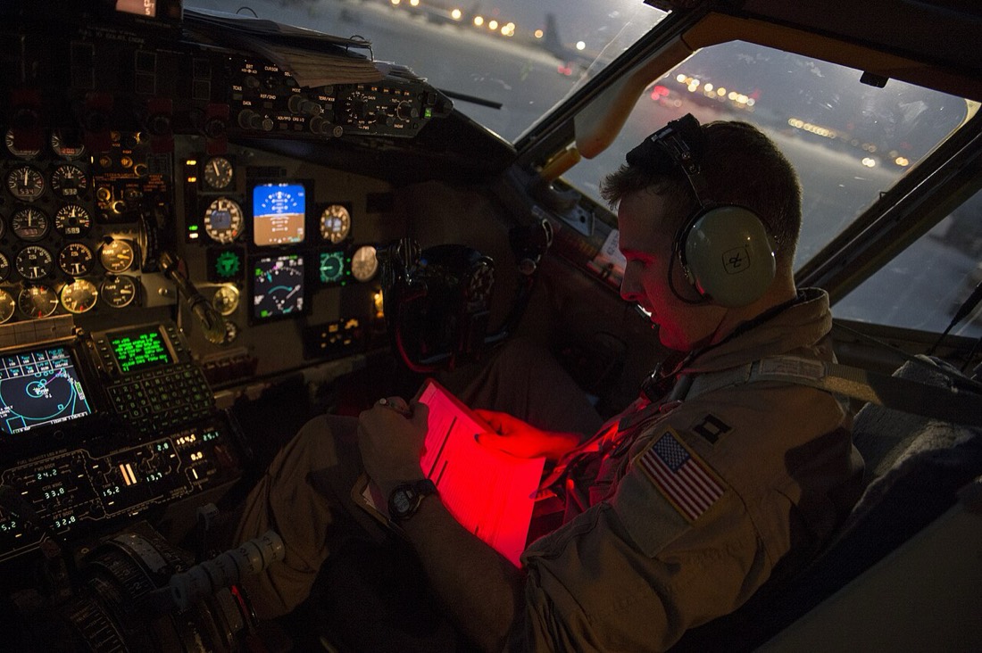 A pilot in a dark cockpit reading a checklist under a red light