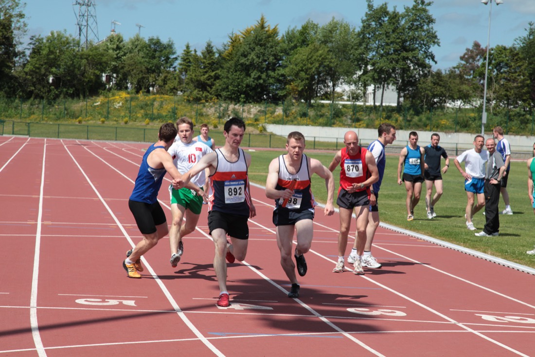 Two runners passing a relay baton on a red athletics track